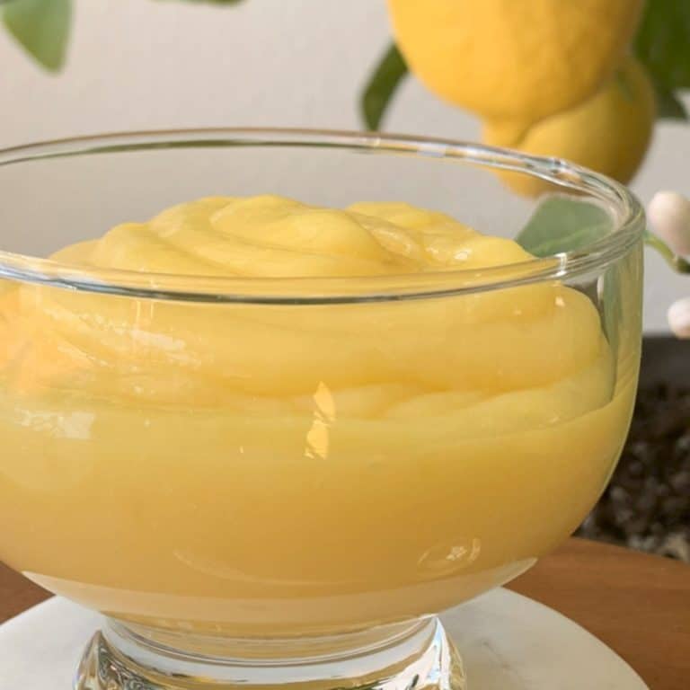 Lemon curd in a glass bawl and a lemon in a background.