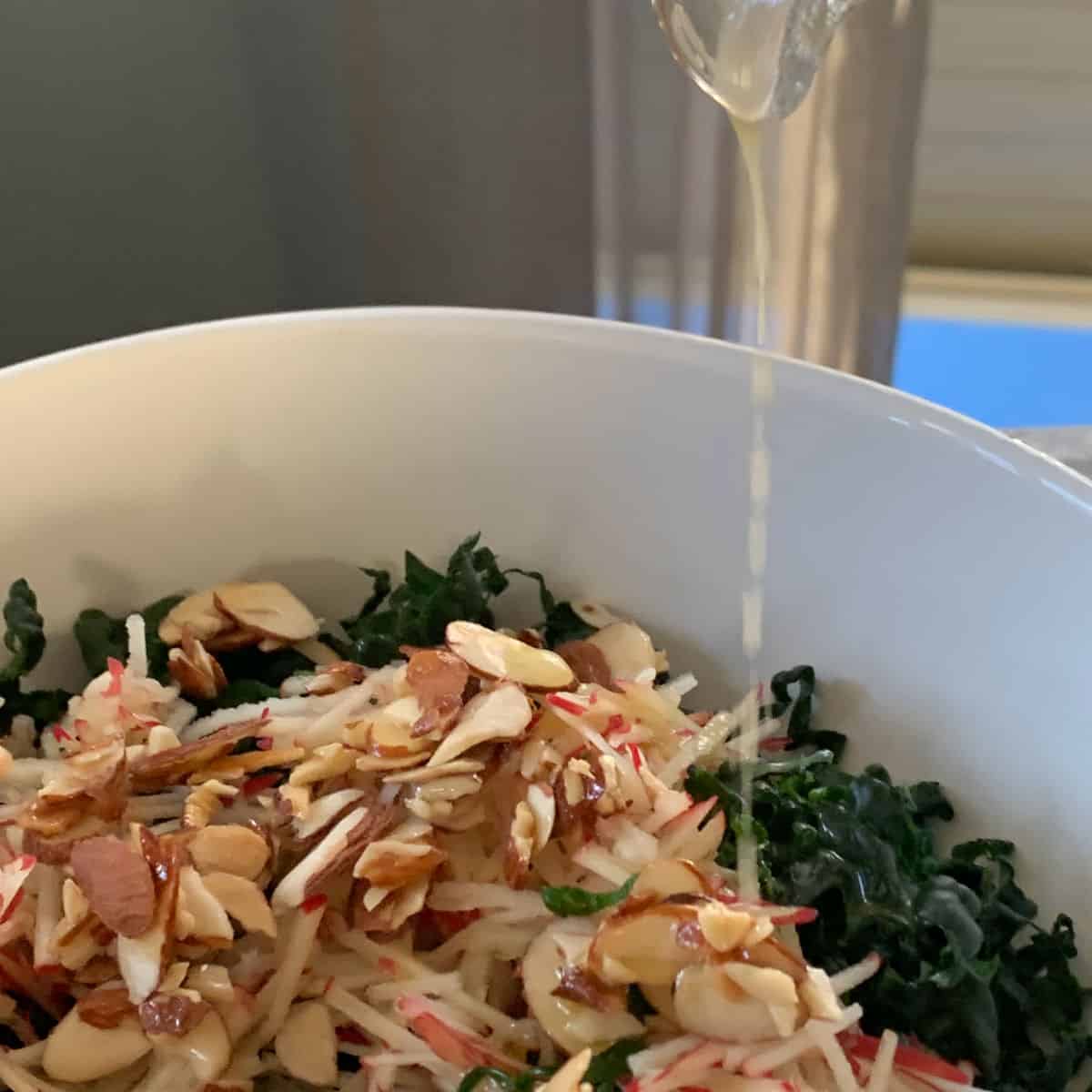 Dressing is being poured over the kale, shredded apples, and almond praline. 