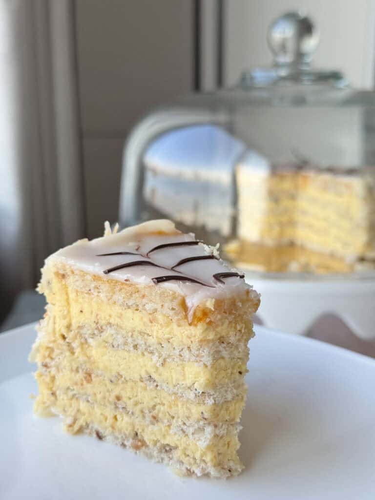 A slice of Esterházy Torte and  a cloche on the background. 