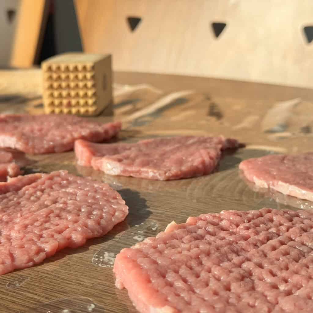 A group of raw meat on a table with meat mallet. 