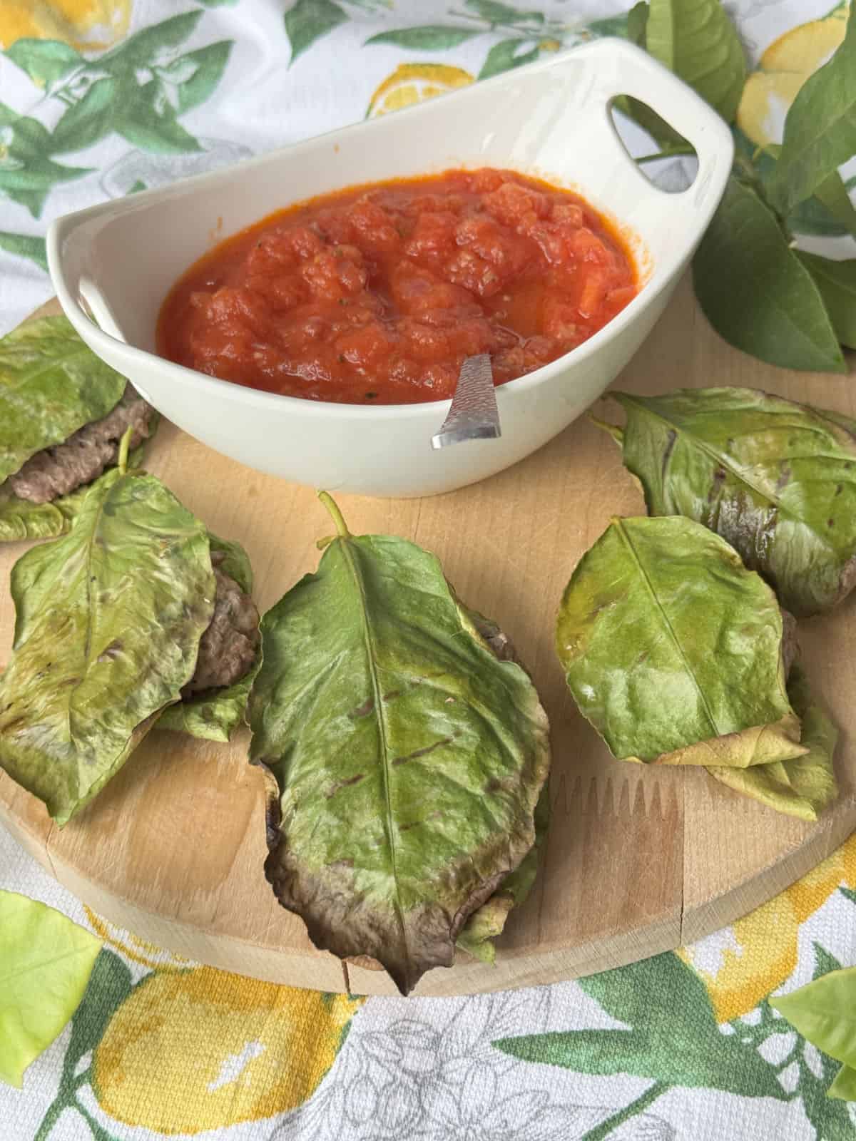 Lemon leaf wrapped meatballs on a wooden board with red tomato sauce.