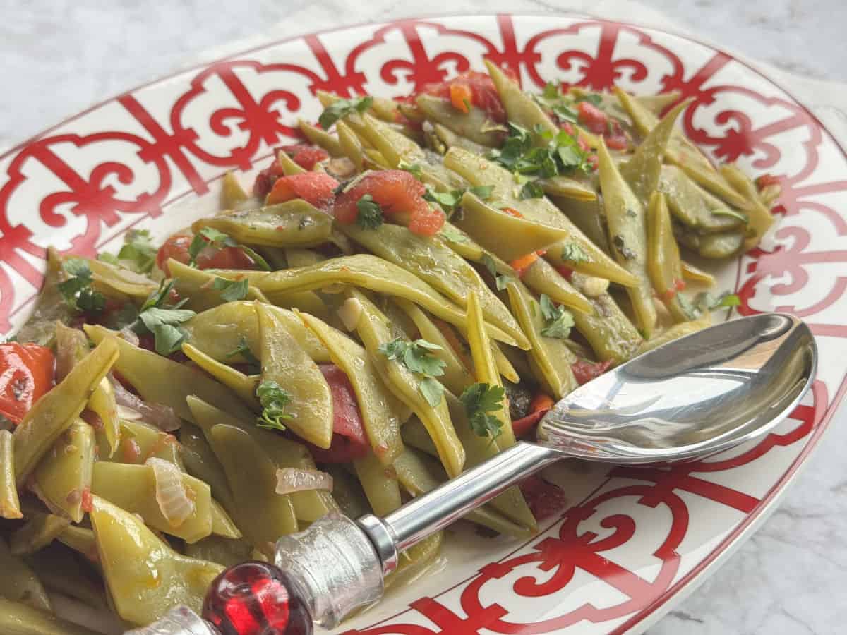 A top-down view of green beans, garnished with fresh herbs and spices.