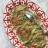 An overhead shot of a beautifully plated green beans with tomatoes arranged on a red plate.