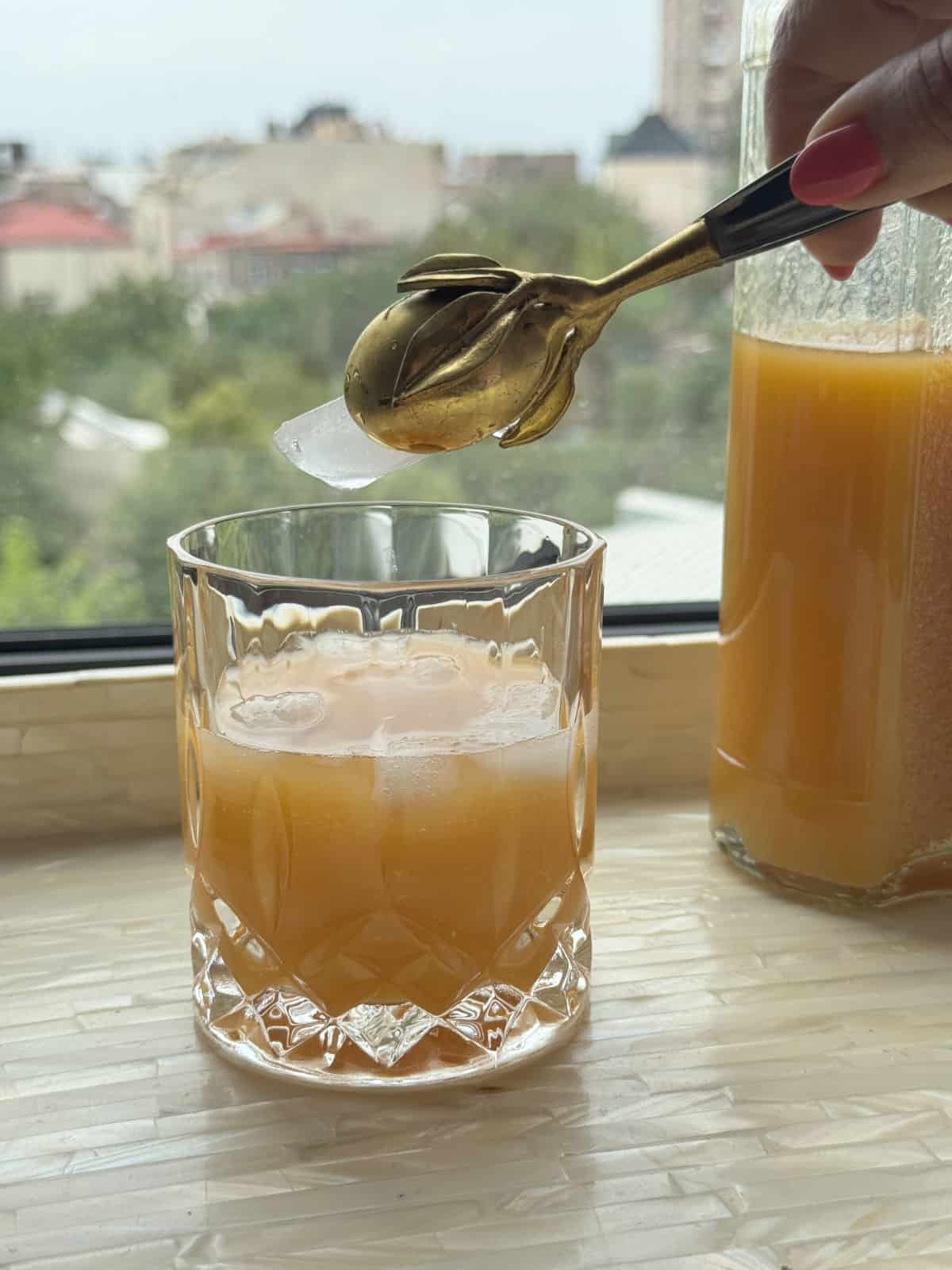 Adding a piece of ice cube to the glass of apricot nectar.