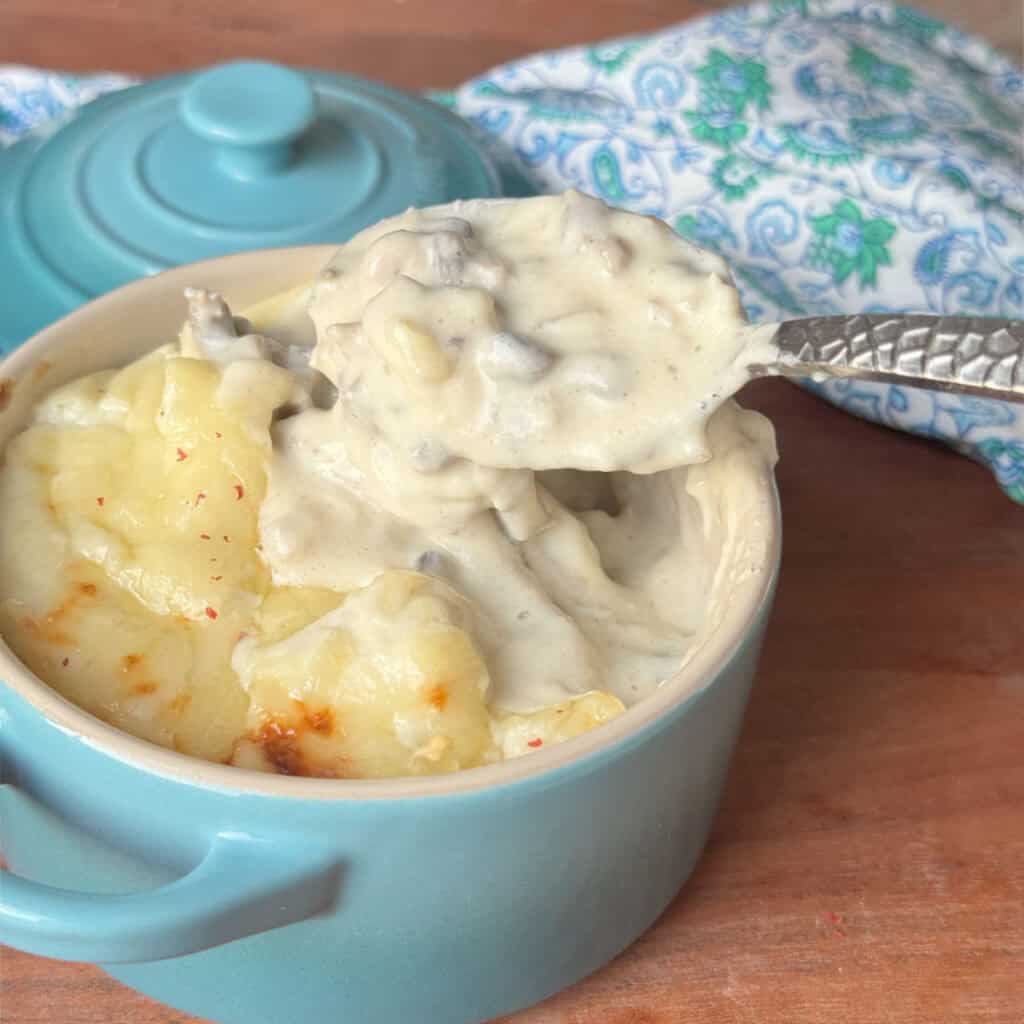 A spoon scooping a portion of chicken julienne in a turquoise blue ramekin revealing its creamy, rich texture.