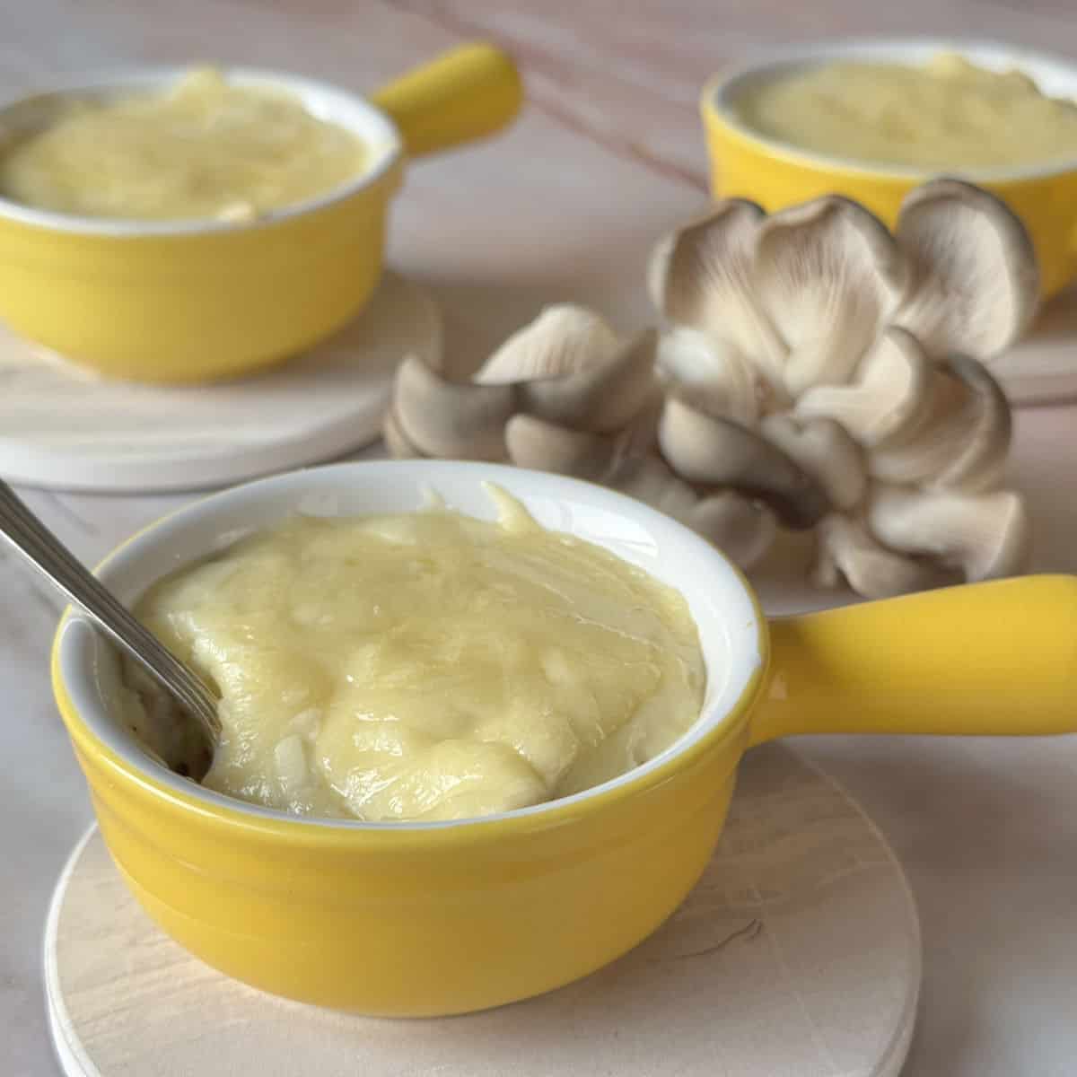 Creamy mushroom soup in yellow mug with fresh mushrooms on side, perfect for cozy cafe dining.